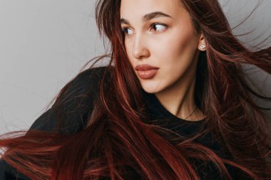 Stüdyoda poz veren kızıl saçlı güzel bir kadın. Açık tenli, düşünceli, siyah bluz ve gümüş küpeler takan kadın modelin yakın plan portresi..