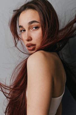 Uzun dalgalı saçlı, doğal makyajlı, çıplak omuzlu genç bir kadın. Moda, güzellik ve günlük tarz yumuşak ışıklandırma ve kapalı stüdyo ortamında kendine güvenen görünüm.