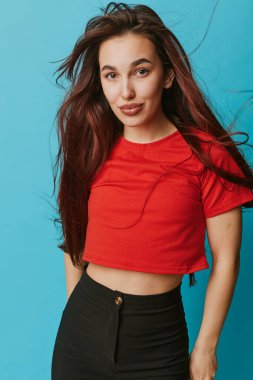 Genç bir kadın portresi, kırmızı kırmız bluzlu dalgalı saçlar ve mavi arka planda duran siyah pantolonlar. Şık bir kıyafet, rahat bir poz, doğal güzellik ve stüdyo ortamında kendine güvenen bir hava..