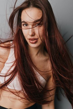 Akan kızıl saçlı, minimum makyajlı beyaz kolsuz bluz giyen çekici bir kadın model. Stüdyo portresi yumuşak ışıklandırma, doğal görünüş, saç hareketi ve doğrudan göz teması..
