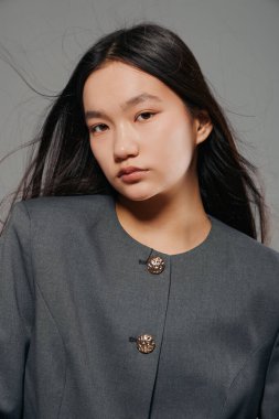 Stüdyoda düz siyah saçlı, gri ceket giyen, doğal makyaj, ciddi görünüş, modern tarz ve moda ve zarafet için minimalist arka plan.