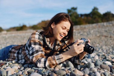 Kayalık plajda bir kadının portresi, bir kamera, orta çekim, neşeli ve rahat açık hava sahneleri, doğa, ve deniz manzaraları, parlak gün ışığında belgelenirken..