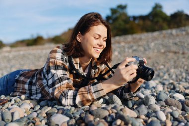 Kayalık bir sahilde kameralı gezgin, rahatlamış ve odaklanmış, manzara, okyanus ufku ve doğa dokularını belgeliyor, amatör fotoğrafçı kıyı ortamının tadını çıkarıyor ve canlı güneş ışığının tadını çıkarıyor..