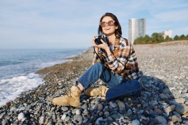 Kayalık bir plajda, güneş gözlüğü, kot pantolon ve fanila ile okyanus esintisinin ve kıyıya yakın parlak gökyüzünün tadını çıkarırken dalgaları ve ufku yakalayan sıradan bir gezgin..