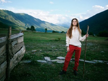 Geniş bir vadide yalnız bir kadın, elinde çalışanlar, beyaz süveter ve kırmızı pantolon, keşfin altını çiziyor, doğa, yalnızlık ve geniş kırsal alan.