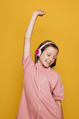 Neşeli genç kız gündelik giysiler içinde kulaklıkla müzik dinliyor gözleri kapalı ve kollarını kaldırmış. Sarı arka plan. Mutluluk, eğlence ve müzik zevki kavramı.
