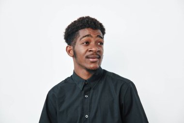 Koyu tenli, kıvırcık saçlı, siyah gömlekli, yandan bakan Afrikalı bir genç. Beyaz arka plandaki stüdyo portresi doğal ifade ve günlük kıyafetleri gösteriyor.
