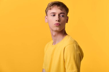 Tek renkli sarı bir sahnede sarı gömlekli sıradan erkeksi bir stil, ifade edici somurtma ve kendine güvenen duruş, stüdyo atmosferi, modern trend, moda hikayeleri için enerjik ve canlı kompozisyon