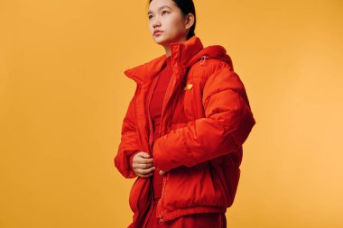 Parlak turuncu ceket ve kazak giyen kadın manken, sarı arka planda fermuarlı giysiler giyiyor, sıcak kış kıyafetleri giyiyor ve sıradan soğuk hava modası sergiliyor..