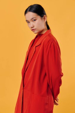 Kırmızı elbiseli düşünceli genç bir kadının portresi. Sarı arka planda elleri ile poz veriyor. Modern moda stüdyosunda güven, tarz ve sakin bir ifade sergiliyor..