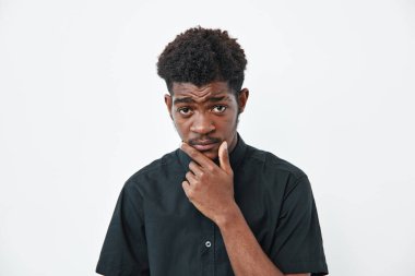 Koyu tenli, siyah tişörtlü, elleri çenesinde, beyaz arka planda ifade veren Afrikalı genç bir adam. Ciddi zenci erkek portresi..