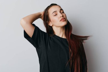 Uzun düz saçlı, siyah gömlekli, gözleri kapalı ve elleri başının arkasında duran genç bir kadın. Doğal makyajlı sakin bir kadın portresi ve hafif arka planda günlük kıyafetler..