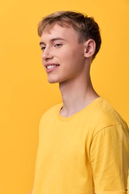 Hafif tebessümlü, tek renkli sarı palet, stüdyo ışıklandırması, ekomünikasyon için uygun temiz kompozisyon, yaşam tarzı kampanyaları ve ürün vitrinleri olan genç bir adamın olduğu sıradan bir moda sahnesi.