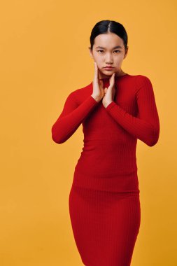 Parlak turuncu arka planda uzun kollu kırmızı elbiseli genç bayan modelin portresi. Moda fotoğrafçılığında eli yüzü düzgün poz veren zarif bir kadın..