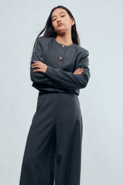 Kendine güvenen, kömür takım elbiseli, kolları çapraz duran, profesyonel iş kıyafetlerini ve modern tarzını gösteren bir kadın. Minimalist geçmişe sahip moda portresi, giyimde güçlendirme ve zarafet.