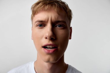 Ani bir anda afallayan genç bir adamın kapanışı, geniş gözler, açık ağız, stüdyo ışıkları, nötr arka plan, canlı dokular ve dramatik ruh hali, çağdaş stok fotoğrafı hissi.