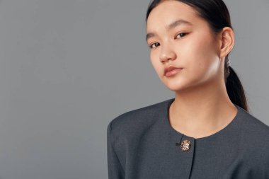 Siyah saçlı Asyalı kadın at kuyruğu takmış resmi koyu giysiler giymiş gri arka planda sakince poz veriyor vesikalık veya kurumsal profil için..