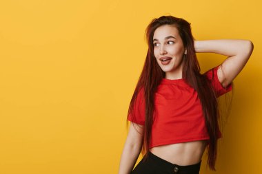 Sarı duvarda duran kırmızı tişörtlü, uzun saçlı, gülümseyen genç kadının portresi. Moda, mutluluk ve rahat poz. Yaşam tarzı ve gençlik konsepti için kafa kafaya..