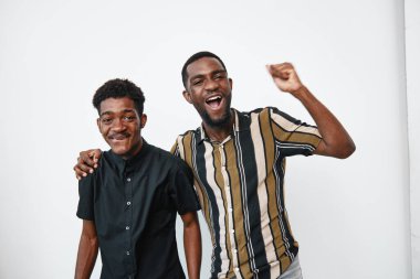 Siyah tenli iki siyah adam birbirine yakın duruyor ve beyaz arka planda günlük gömleklerle gülümsüyor. Arkadaşlık, mutluluk, neşe ve kutlama. Olumlu duygular ve günlük yaşam tarzıyla birlikte..