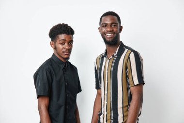 Siyah tenli Afro-Amerikalı erkekler günlük gömleklerle poz veriyorlar, beyaz arka planda stüdyo dekorları, arkadaş canlısı ifadeler ve yaşam tarzı konsepti için rahat duruş..