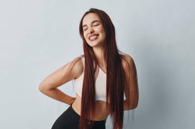 Uzun örgülü spor elbiseli, taytlı, elleri arkada, gözleri kapalı gülümseyen bir kadın. Spor modeli, sağIık, sağlık, egzersiz ve hafif stüdyoda günlük portre.