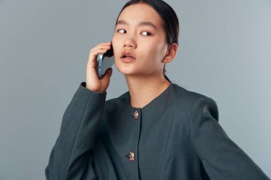 Gri ceketli, kulağına yakın bir yerde telefonu tutan iş kadını, tarafsız stüdyo arka planında ciddi bir yüz ifadesiyle yan bakıyor. Genç yetişkin kadın cep telefonuyla konuşuyor şirket veya kişisel kullanım için..