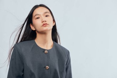 Gri ceketli, uzun siyah saçlı, sakin ve kendinden emin genç bir kadının portresi..