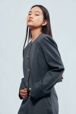 Uzun düz saçlı, koyu renk ceketli, açık arkaplanda poz veren kendine güvenen genç bir manken. Ciddi yüz ifadesi ve duruş şekli olan şık giyinmiş bir kadın..