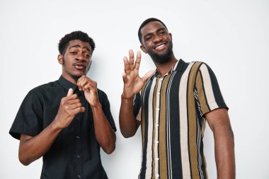 Siyah tenli iki siyah adam beyaz arka planda yan yana duruyor. Sıradan tarz, gülen yüzler, el hareketleriyle dostluk ve mutluluk ve stüdyo ortamında rahatlama havası..
