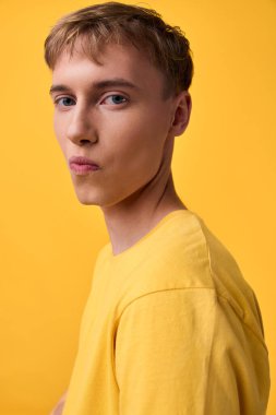 Stüdyoda tek renkli arka plan, yakın çekim, sakin titreşim, temiz kompozisyon, günlük moda ürünleri olan sarı tişört giyen bir erkek.