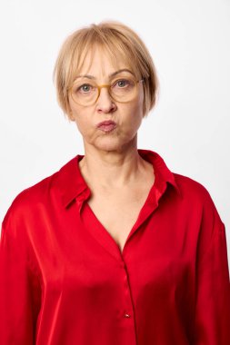 Kırmızı gömlekli, kısa sarı saçlı ve gözlüklü orta yaşlı bir kadın beyaz arka planda neşeli bir yüz oluşturur. Mizah, ifade, kişilik ve günlük tarz kavramı.