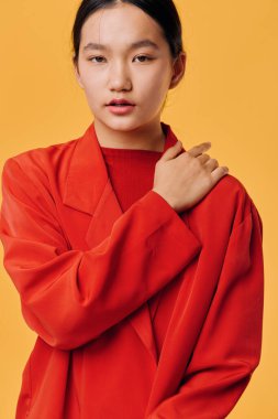 Sarı arka planda gevşek turuncu ceket giyen genç kadın modelin portresi, el ele ve moda tarzı için ince makyajlı rahat pozlar gösteriyor..