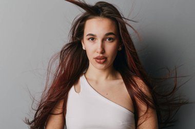 Beyaz bluzlu, dalgalı kahverengi saçlı genç bir kadının portresi. Ciddi bir ifadeyle kameraya bakıyor. Yüzünde doğal ışık var..