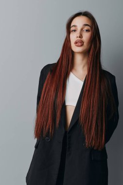 Siyah ceketli, uzun düz kızıl saçlı ve beyaz gömlekli gri arka planda poz veren genç bir kadın. Moda ve güzellik konsepti için doğal görünümlü şık bir kadın modeli..
