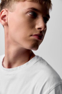 Düz beyaz tişörtlü genç bir adamın profili, sakin bakışlar yana, dramatik ışıklandırma ve pürüzsüz ten rengi yaşam tarzı, moda veya reklam projeleri için ideal.