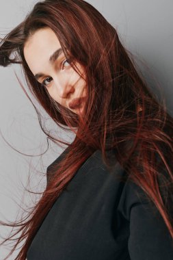 Akan kızıl saçlı ve minimum makyajlı bir kadın model. Yakın plan portre ve modern saç stili konsepti için gri duvara siyah bir bluz giyiyor..