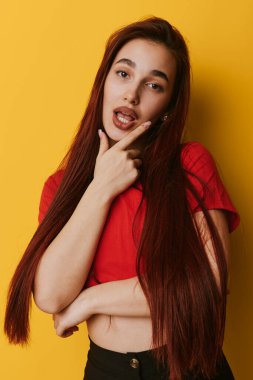 Uzun düz saçlı, kırmızı saçlı genç bir kadının portresi. Eli çenesinde, düşünceli bir yüzü var. Moda ve yaşam tarzı için parlak sarı bir arka planı var..