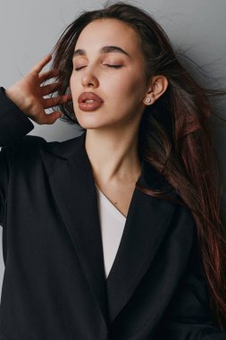 Kapalı gözlü ve rahat yüzlü genç bir kadın modelin portresi, siyah giyimli, dokunaklı saçlar, gösterişli güzellik ve zarafet nötr zemin üzerinde minimalist tarzda.