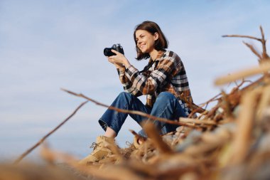 Açık hava fotoğrafçıları bir kumulda dinleniyor, kamera elinde, uzun otların ve açık gökyüzünün ortasındaki doğa ve manzara sahnelerine odaklanmış durumda..