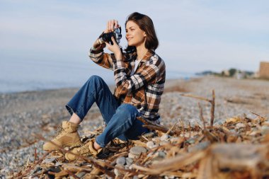 Sahil şeridindeki profesyonel fotoğrafçı, ekose gömlek ve kot giymiş bir kamerayla okyanusu fotoğraflıyor, sakin doğanın ve açık hava manzarasının tadını çıkarıyor..