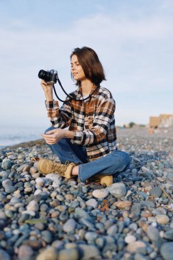 Kayalık bir sahilde sıradan bir fotoğrafçı, lensler hazır, bir kamera, ekose gömlek, kot ve deniz esintisinin ortasında sakin bir ifade ile sahili belgeliyor..