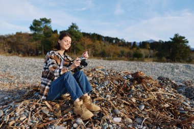 Kayalık bir plajda, sonbahar renklerinde, kot, ekose ve kamera olan bir kadın fotoğrafçıyla açık hava çekimi sahnesi gizli manzara için hazır..
