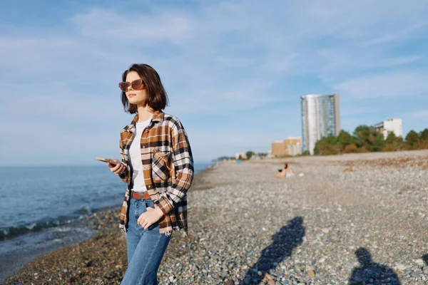 Sahil şeridinde telefon, güneş gözlüğü, kareli gömlek, kot pantolon, suyun esintili günü, uzak gökdelenler ve rahat bir hava yaratıyor..