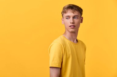 Sarı temalı resim, tek renkli stüdyo ortamında sarı tişört giyen, pazarlama, reklamcılık ve editoryal kullanım için güven, basitlik ve çağdaş tarz taşıyan bir adamı içeriyor.