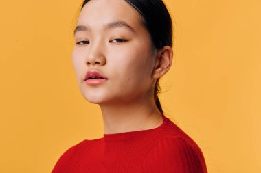 Siyah saçlı, kırmızı elbiseli, parlak sarı arka planda genç bir kadının portresi. Yaşam tarzı veya reklam konsepti için tarafsız yüz ifadesine sahip yakın çekim, güzellik, moda ve zarafet.