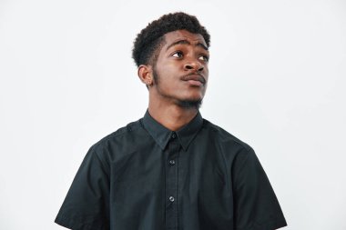 Siyah tenli, kısa kıvırcık saçlı, siyah tişörtlü, beyaz arka plana bakan genç bir adamın portresi. Düşünceli ifadesi ve günlük kıyafetleri olan Afrikalı etnik erkek..