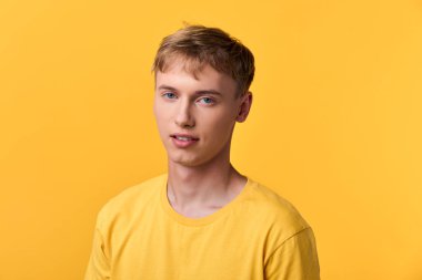 Sarı tişörtlü bir erkek model, saf sarı bir arkaplan, rahat bir ifade, minimal stil, markalaşma, sağIık ve moda kampanyaları için uygun bir stüdyo çekimi önünde duruyor.