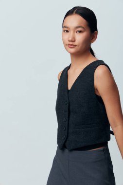 Pürüzsüz saçlı, siyah kıyafetli, kolsuz yeleği ve pantolonu olan Asyalı bir kadın. Rahat duruş ve yumuşak stüdyo ışıklarıyla, rahat bir şekilde ışık perdesine izole edilmiş görünün..