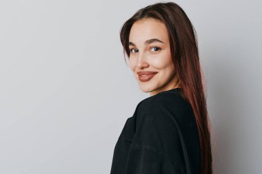 Düz saçlı, siyah bluzlu, gülümseyen kadın portresi kameraya bakıyor. Tarafsız arkaplan, doğal ışık, dostane ruh hali ve yumuşak yüz özelliklerine sahip stüdyo çekimi.