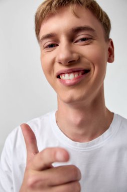 Neşeli bir gülümsemesi ve olumlu bir jesti olan genç bir adam iyimserlik ve motivasyon saçıyor. Temiz bir arkaplan, yumuşak aydınlatma, modern ve kendinden emin görünüm, pozitif mesajlaşma için ideal ve günlük